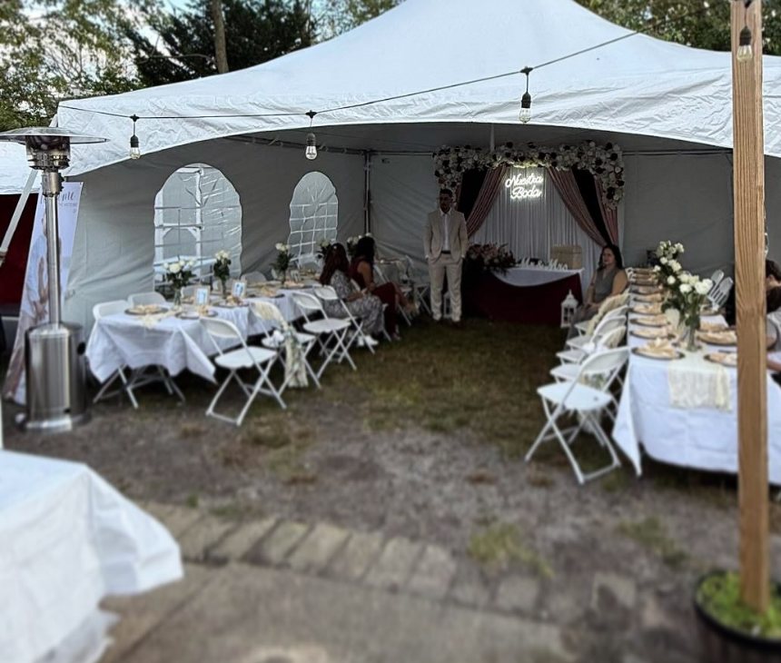 A tent with sidewalls, patio heaters and long tables in white linens set for a fall evening reception.